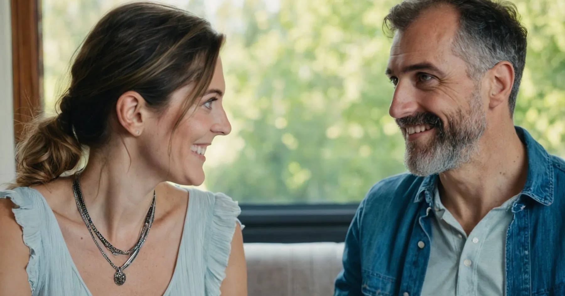 Un homme à la barbe grisonnante et une femme brune se sourient près d'une fenêtre ouverte sur la verdure