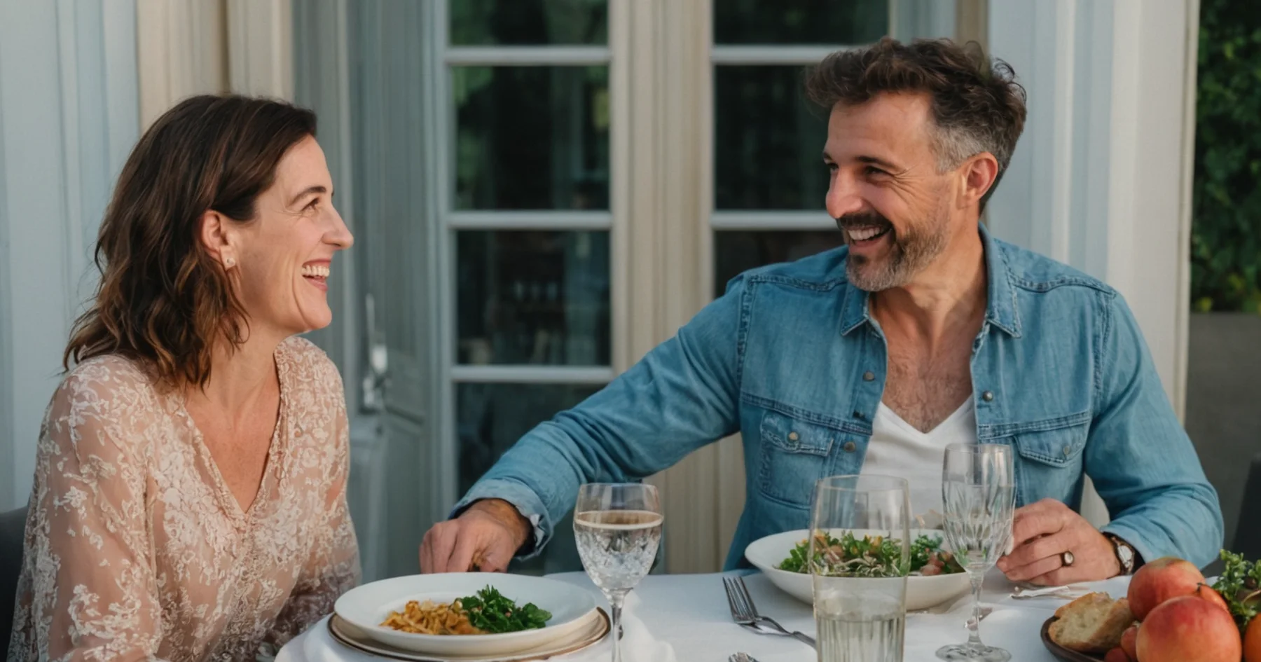 Un couple qui rit en échangeant un regard complice à une table dressée en terrasse